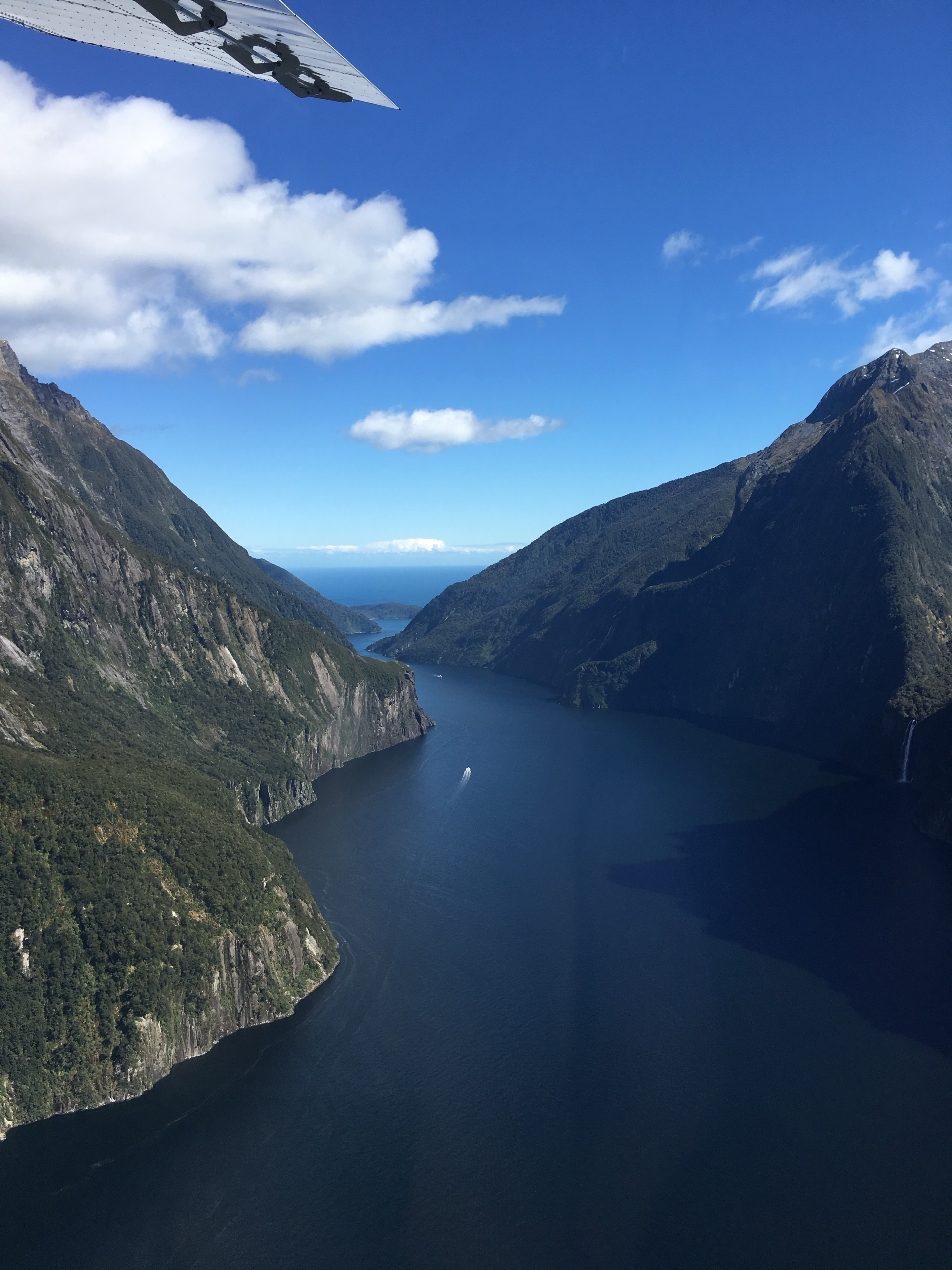 Aerial view of a deep blue waterway between steep green mountains in New Zealand