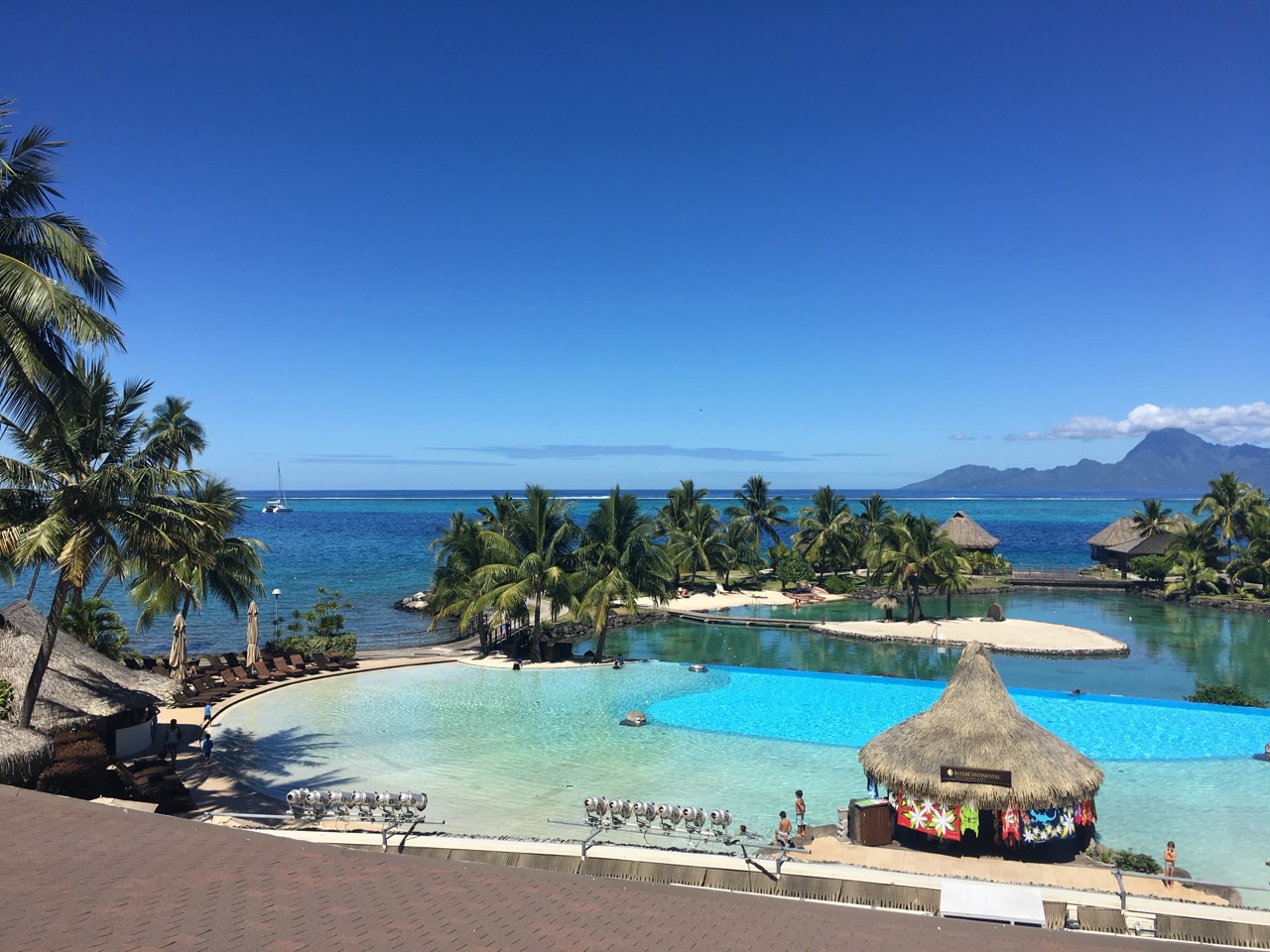 Tahiti resort pools framed by palms, with blue ocean and a mountainous island beyond